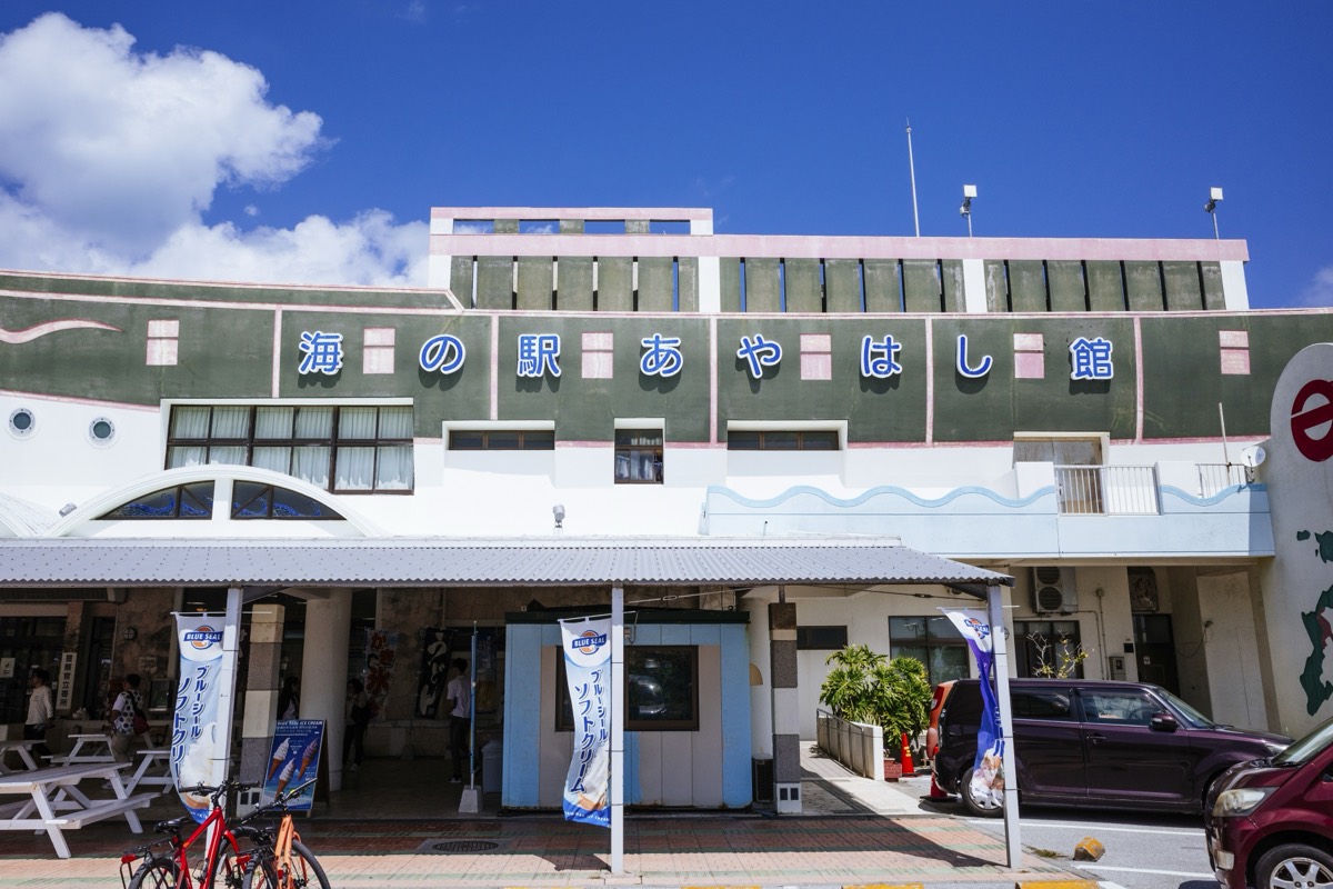 The green facade and blue sign of Umi-no-Eki Ayahashikan with soft-serve banners outside