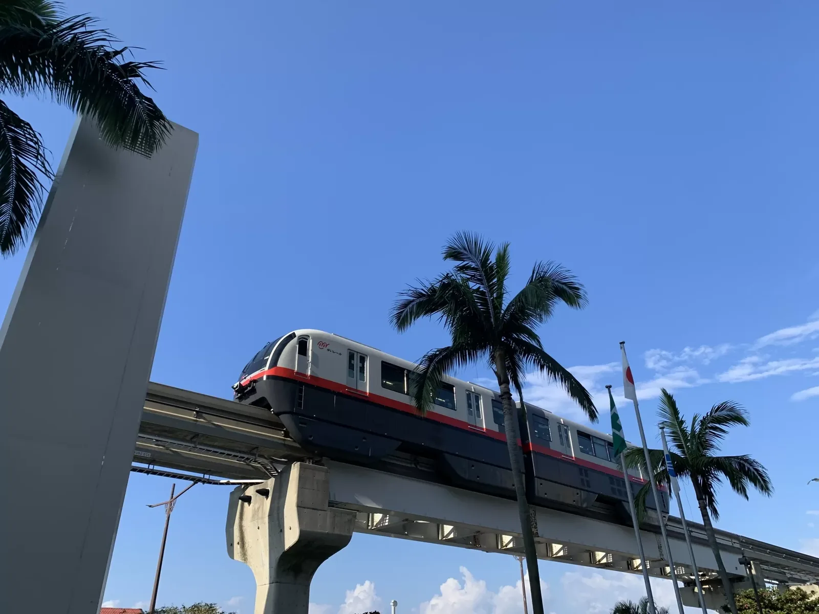 A Yui Rail train on its elevated guideway above palm trees in Naha