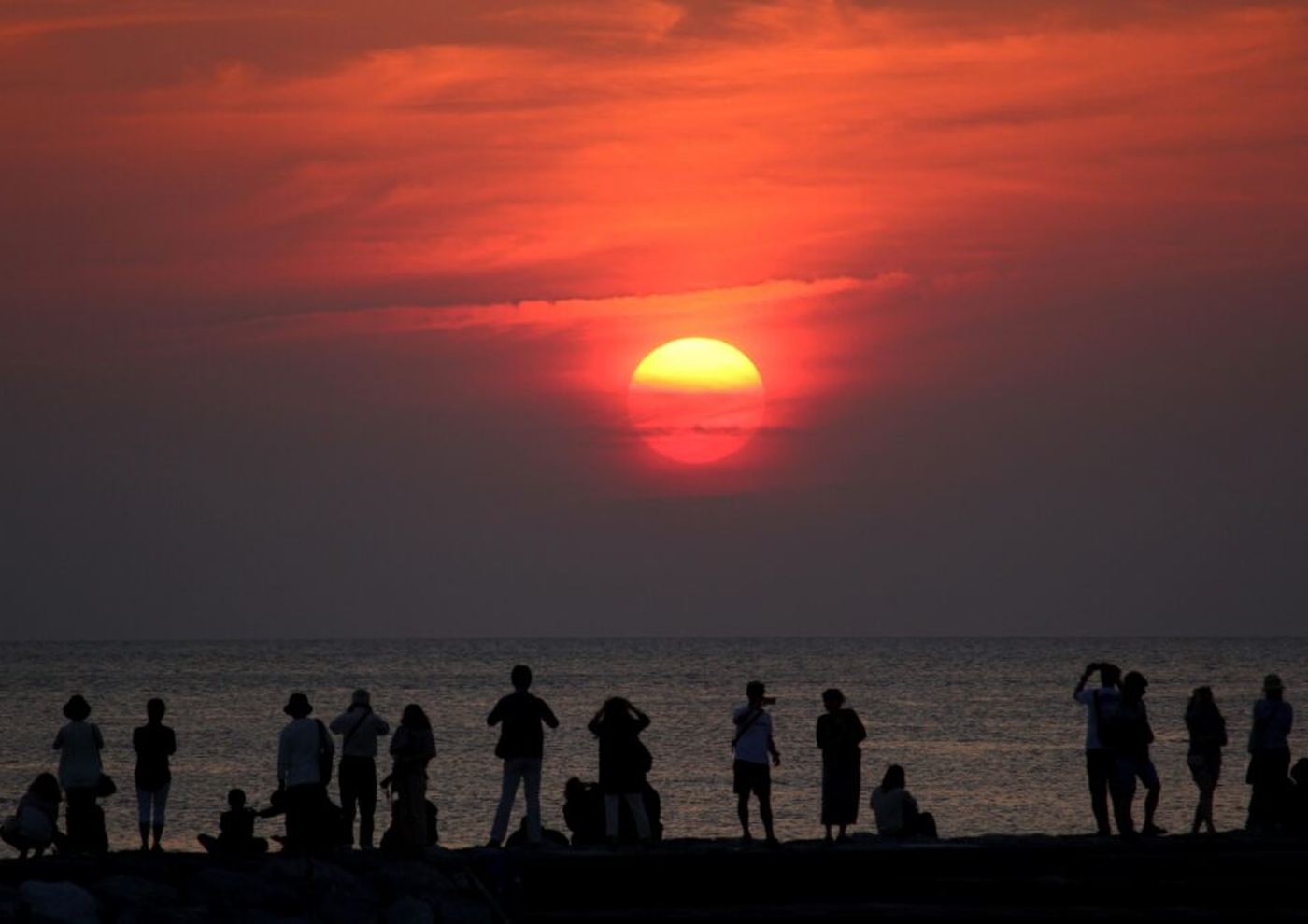 夕日を見に集まった人たちの影が並ぶ砂浜